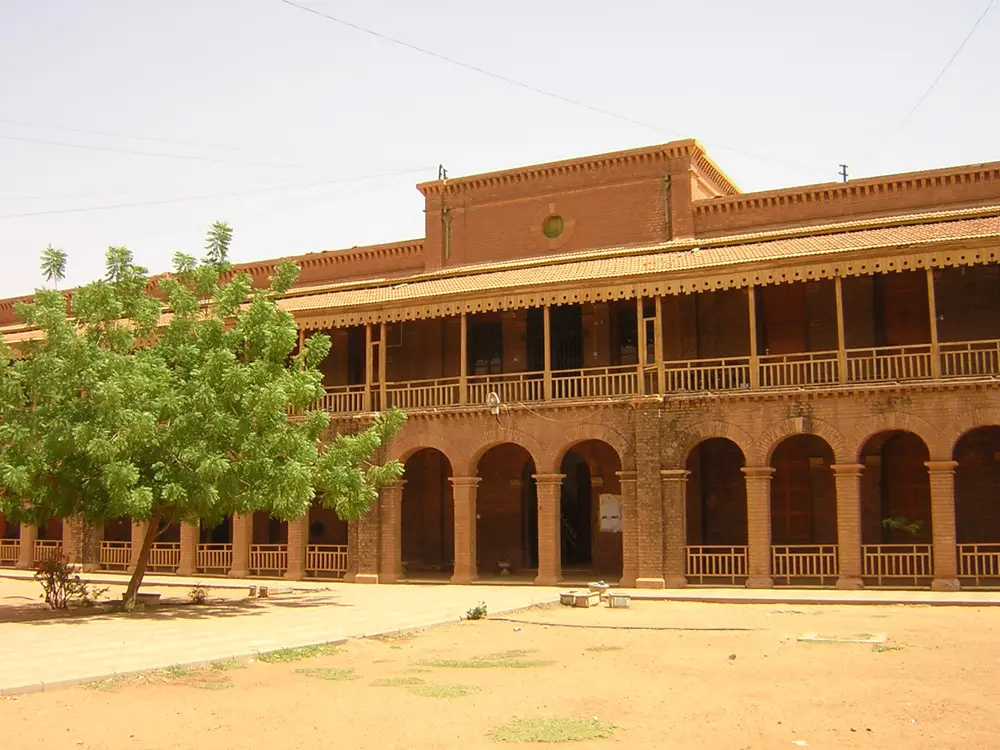 A red-brick campus building with a ground-floor arcade and a wooden balcony